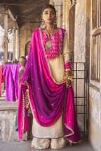 Woman in traditional Indian attire with a pink and purple dupatta and jewelry, standing in an outdoor setting.