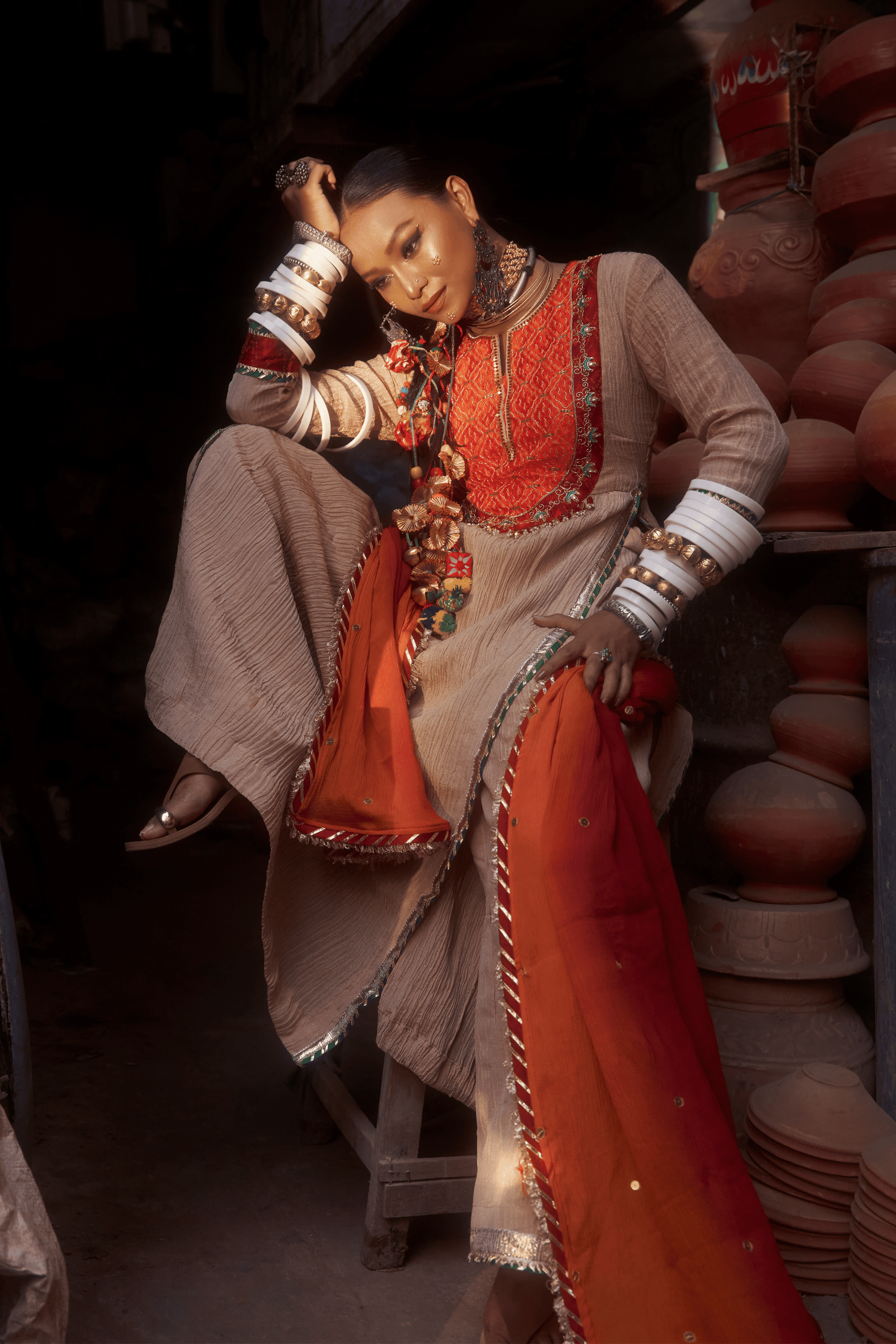 Woman in traditional attire sitting against a backdrop of stacked clay pots.