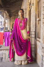 Woman in traditional pink and purple outfit standing in front of a stone building.
