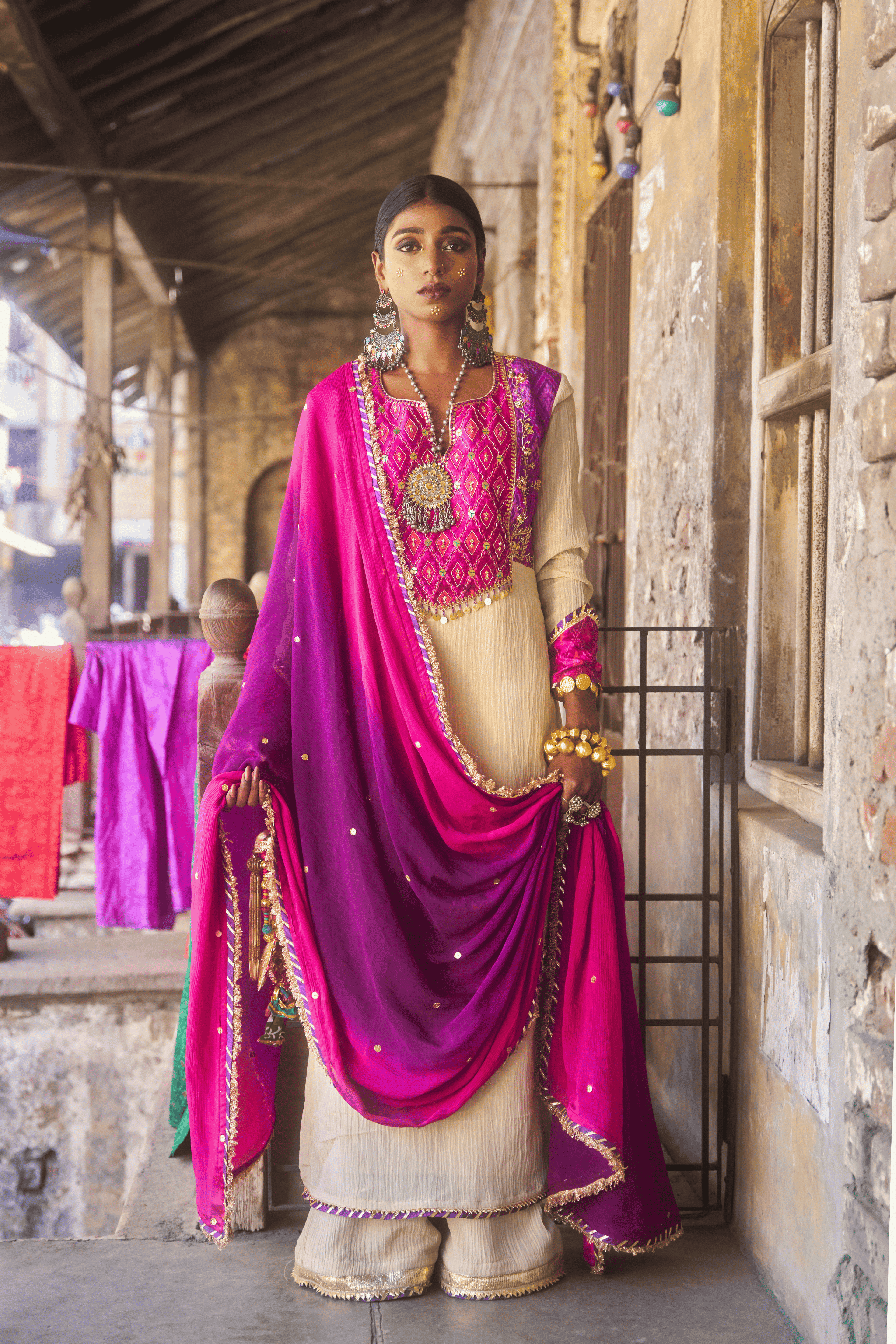Woman in traditional pink and purple outfit standing in front of a stone building.